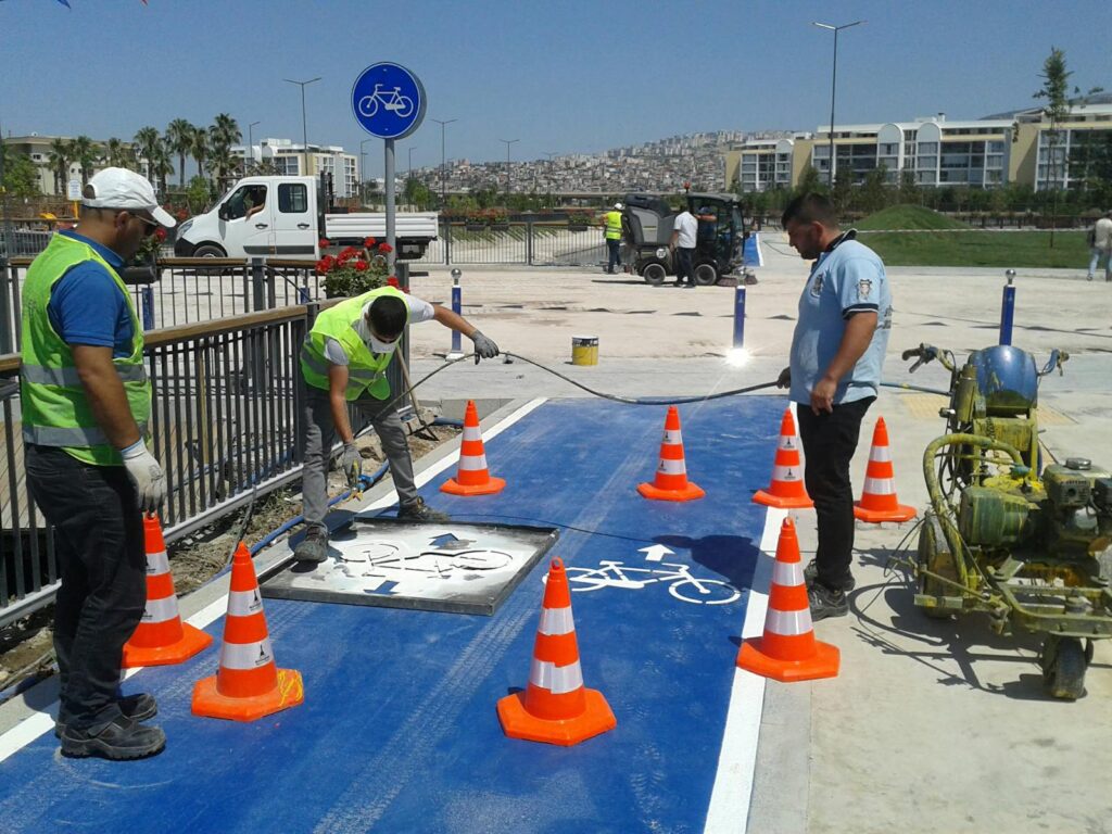 Full body road workers wearing uniforms and high visibility vests marking cycle lane with white paint on sunny weather